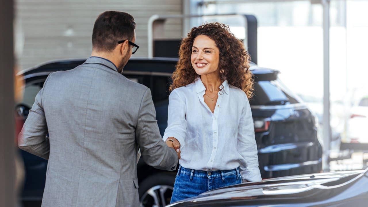 Happy salesman selling the car to his female customer in a showroom.