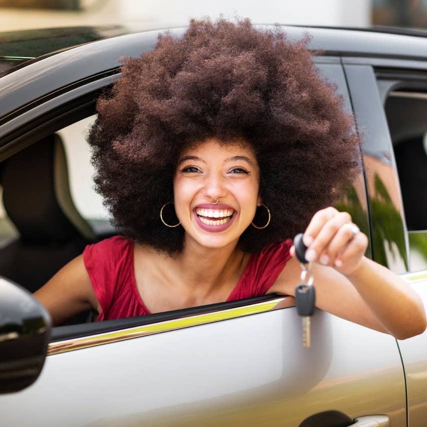 Smiling young woman showing car key while sitting in car