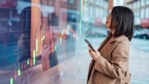Person holding smartphone while looking at large LCD display of a chart.