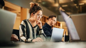 woman looking at laptop in an office with coworkers sitting nearby