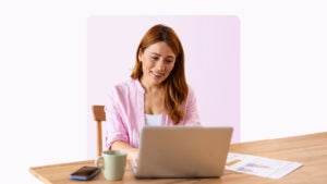 A smiling woman sits at a laptop.