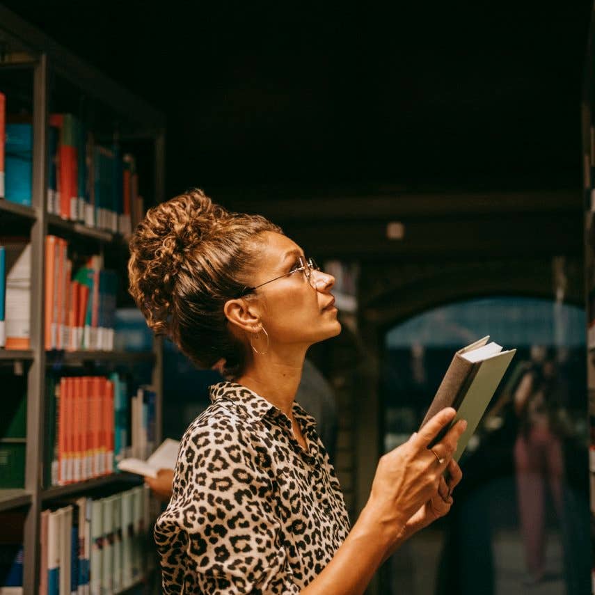 Female university student choosing book from shelf in library