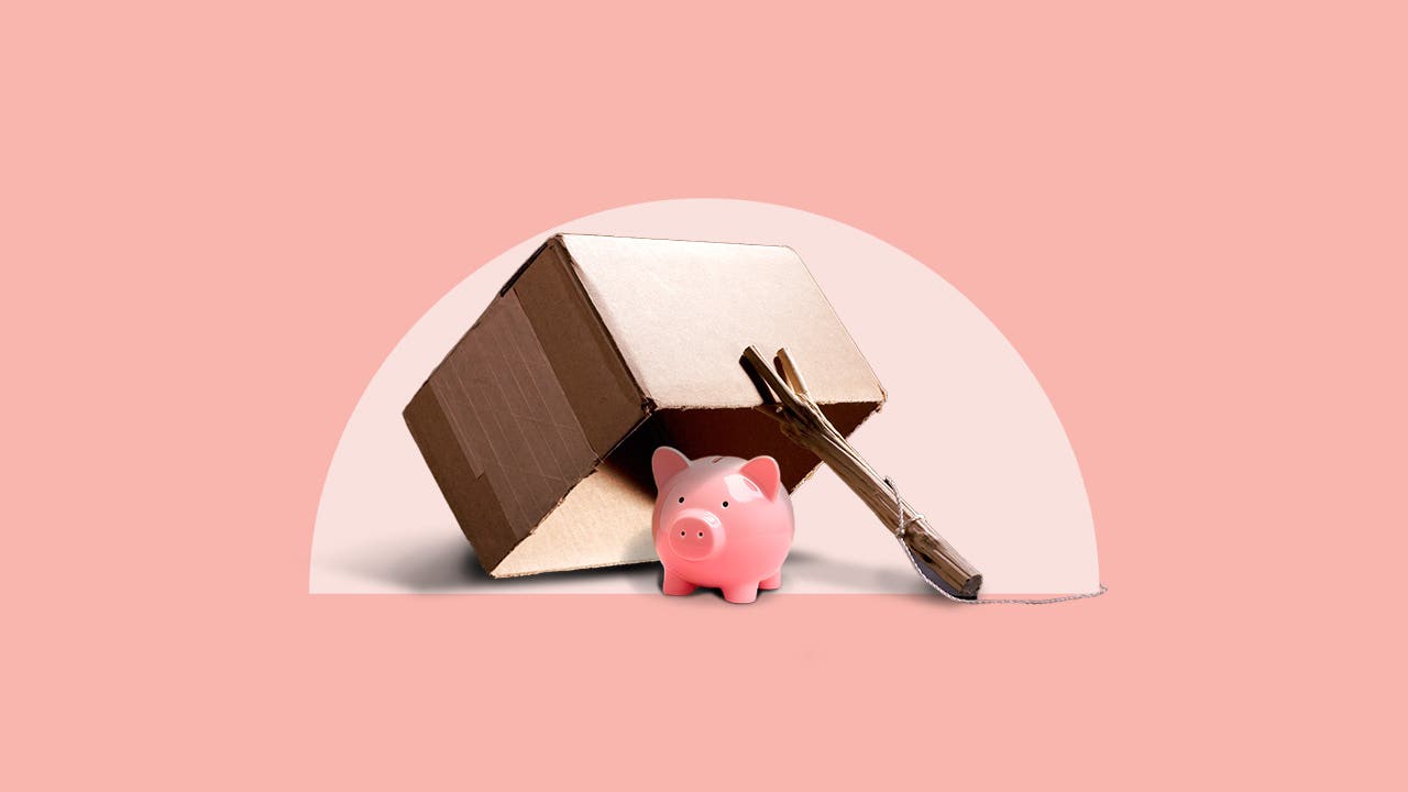A piggy bank sits under a makeshift trap made from a cardboard box and a stick.