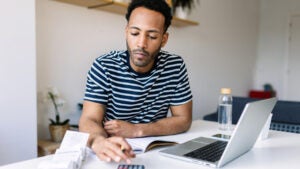 man using calculator and computer to do taxes