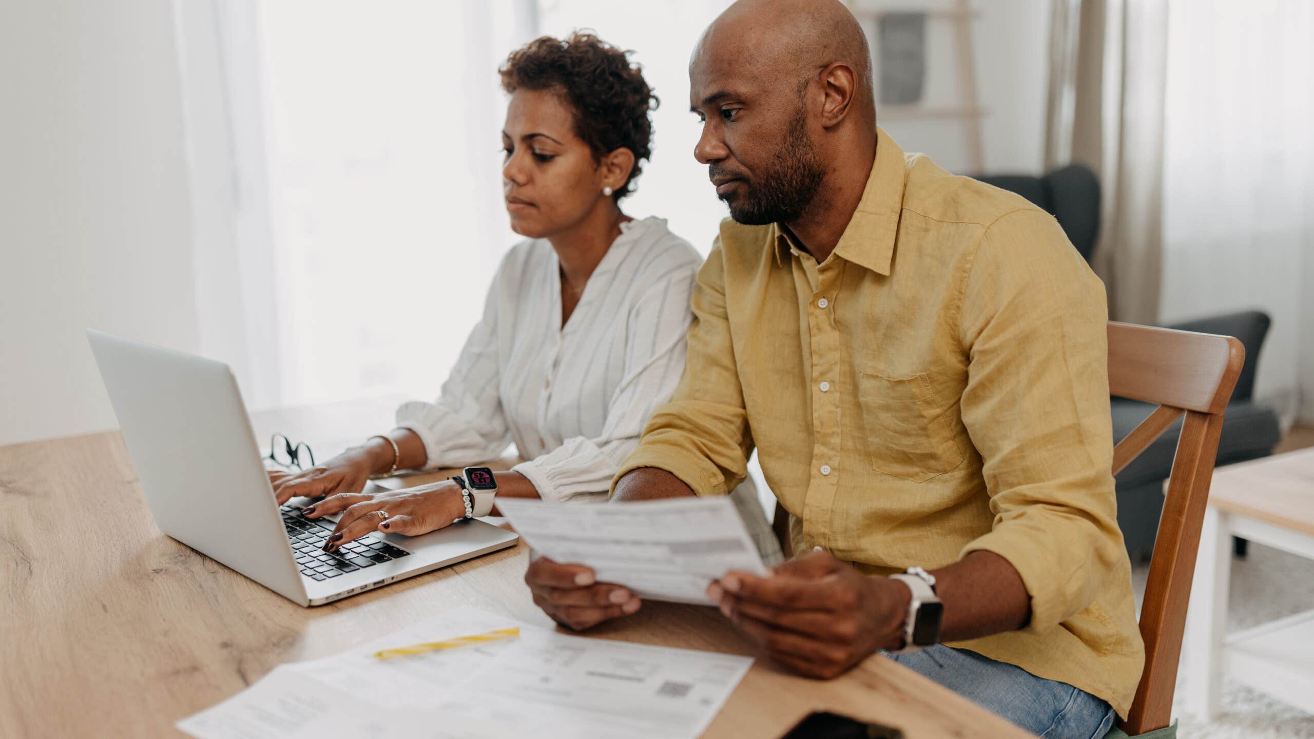 A couple is deeply involved in their financial planning as they work together, using a laptop, and reviewing various documents.