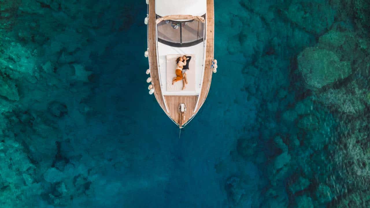 Aerial drone view of couple on board of luxury yacht anchored in tropical paradise bay with emerald clear water