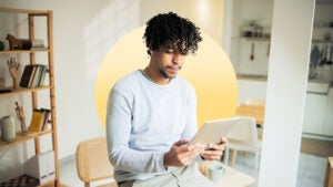 young man sitting in his home reading an electronic tablet