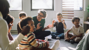 Gray-haired female teacher playing with a group of preschool children.