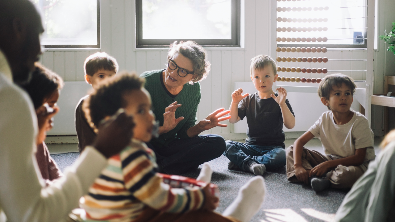 Gray-haired female teacher playing with a group of preschool children.
