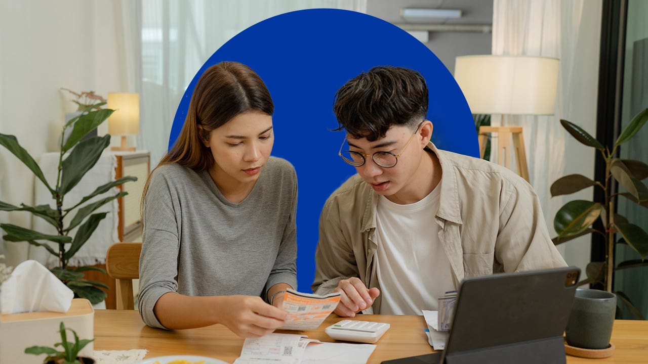 Young couple reviews paperwork at a table, with a laptop open in front of them.