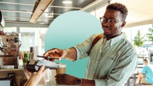 Young black man smiling while paying with a credit card at a coffee shop