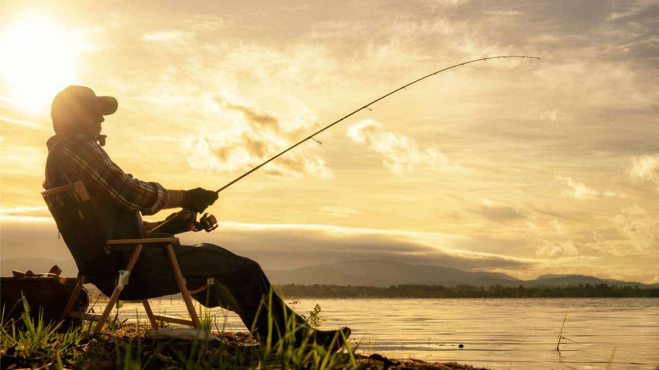A man fishes along the waterfront at sunrise