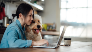A young woman assesses her retirement plan on her laptop with her dog in her lap.