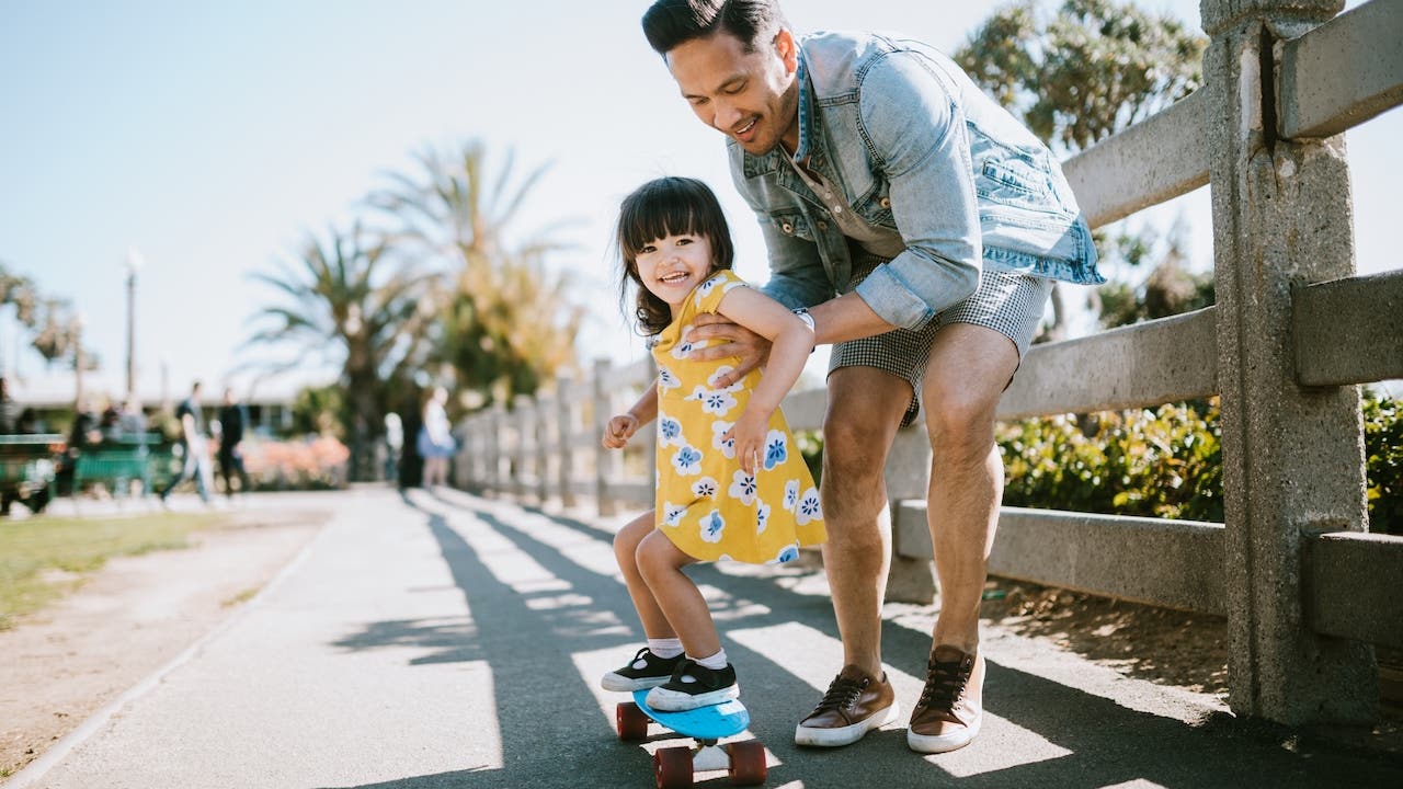 Dad helps young daughter ride skateboard, Father's Day tax tips