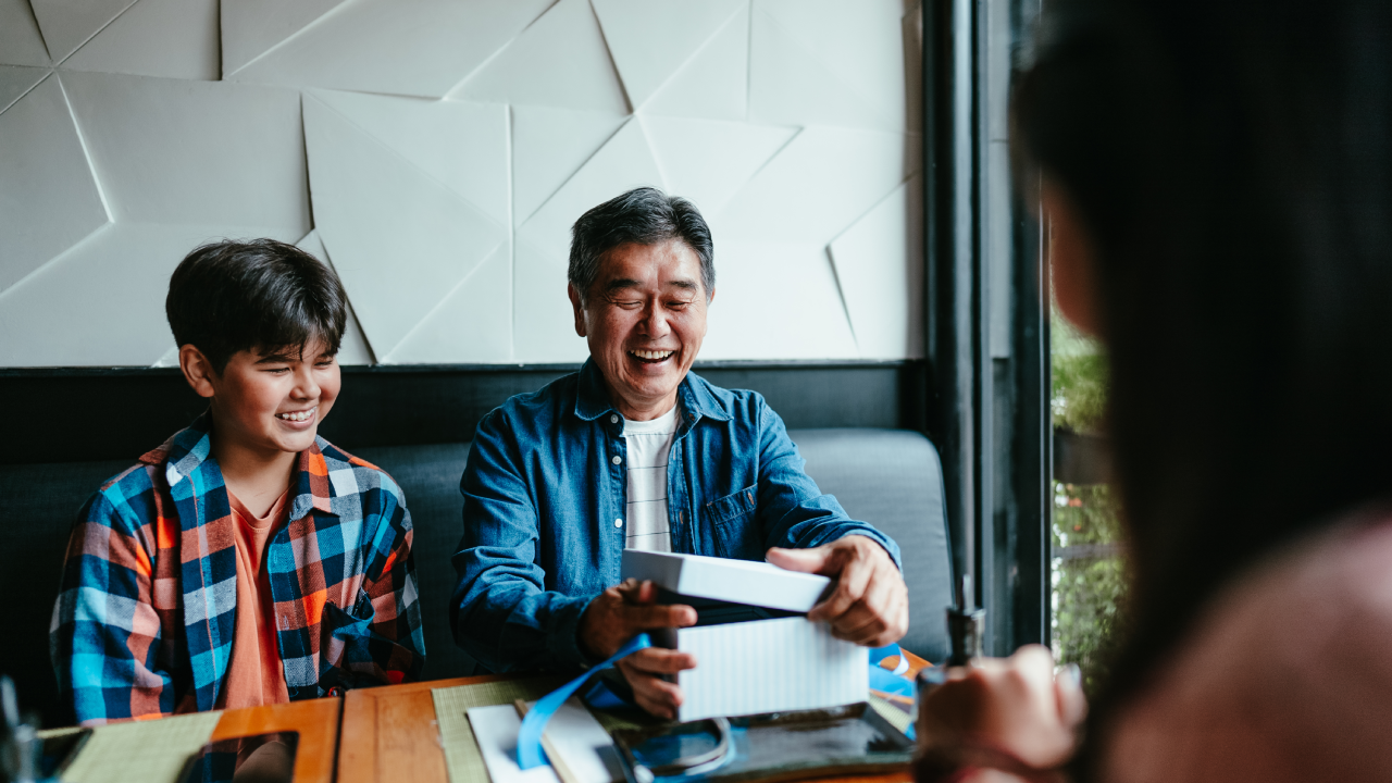 Older man receiving a gift from his family at a restaurant.