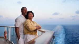 Mature African American couple, standing and leaning on railing on deck of a cruise ship, looking off into the distance.