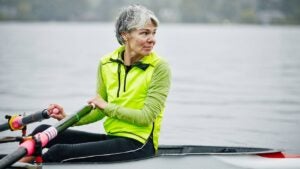 An active senior woman rows a boat on the water.