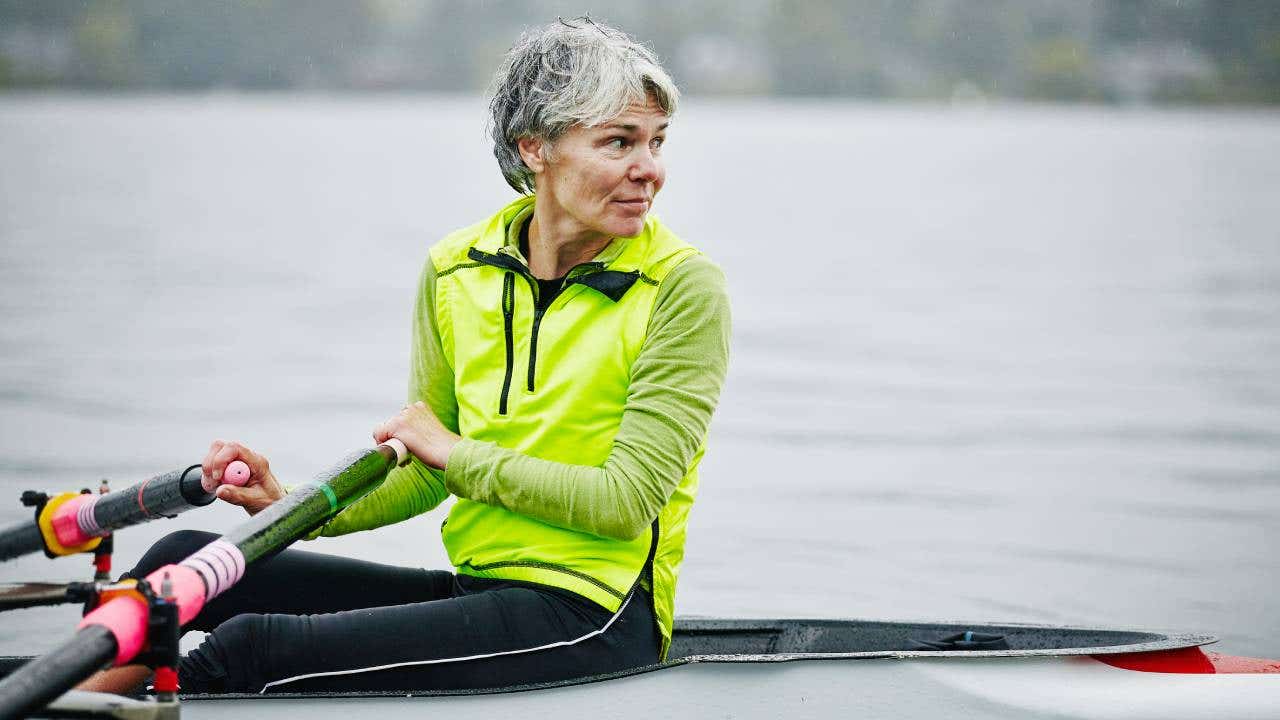 An active senior woman rows a boat on the water.