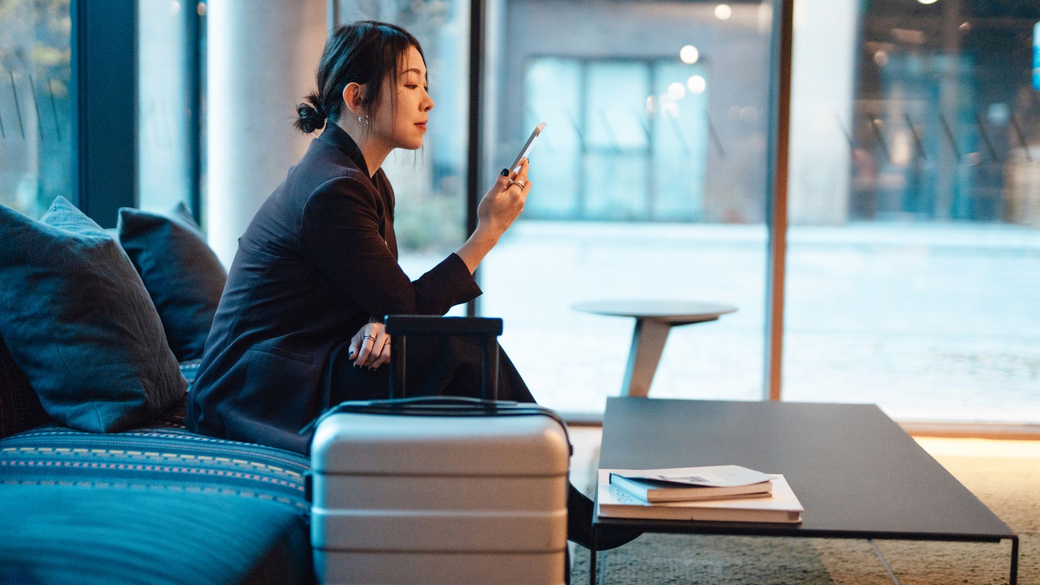 Business woman doing online check-in with smartphone while sitting at hotel lobby, getting ready to depart. Young woman on business trip.
