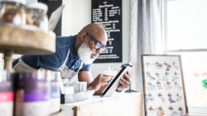 Small-business owner looks at his tablet as he works at the counter of his store.