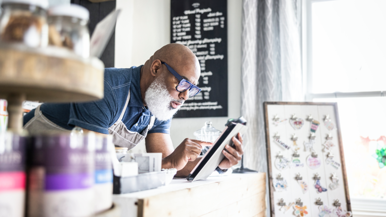 Small-business owner looks at his tablet as he works at the counter of his store.