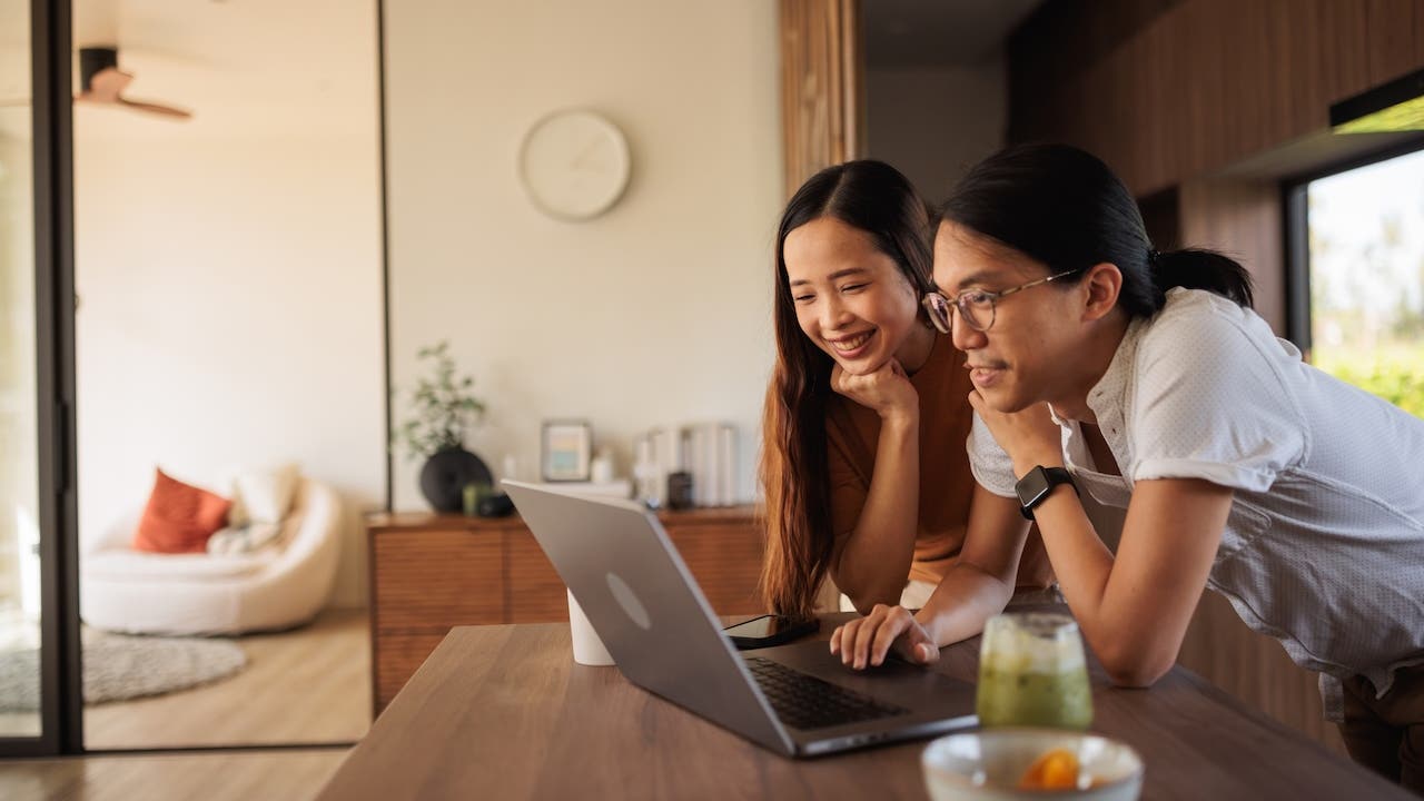 smiling asian couple looking at laptop in kitchen
