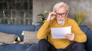 A retirement-age man reads a letter on his couch.
