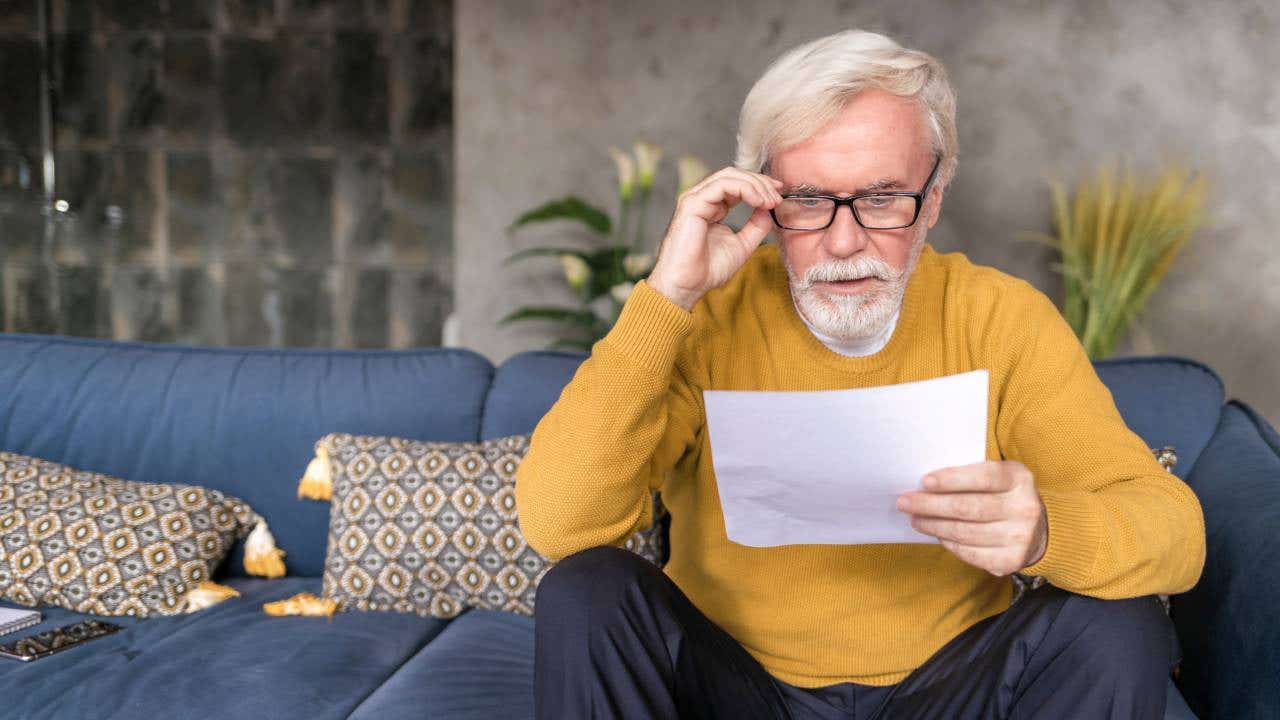 A retirement-age man reads a letter on his couch.