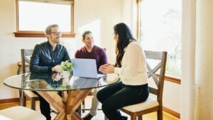 Two men discuss estate planning with a financial advisor at their kitchen table.