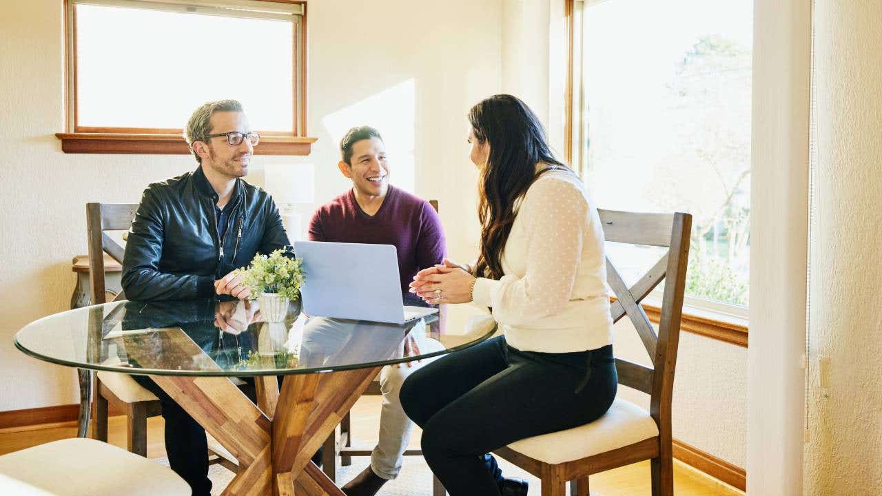 Two men discuss estate planning with a financial advisor at their kitchen table.
