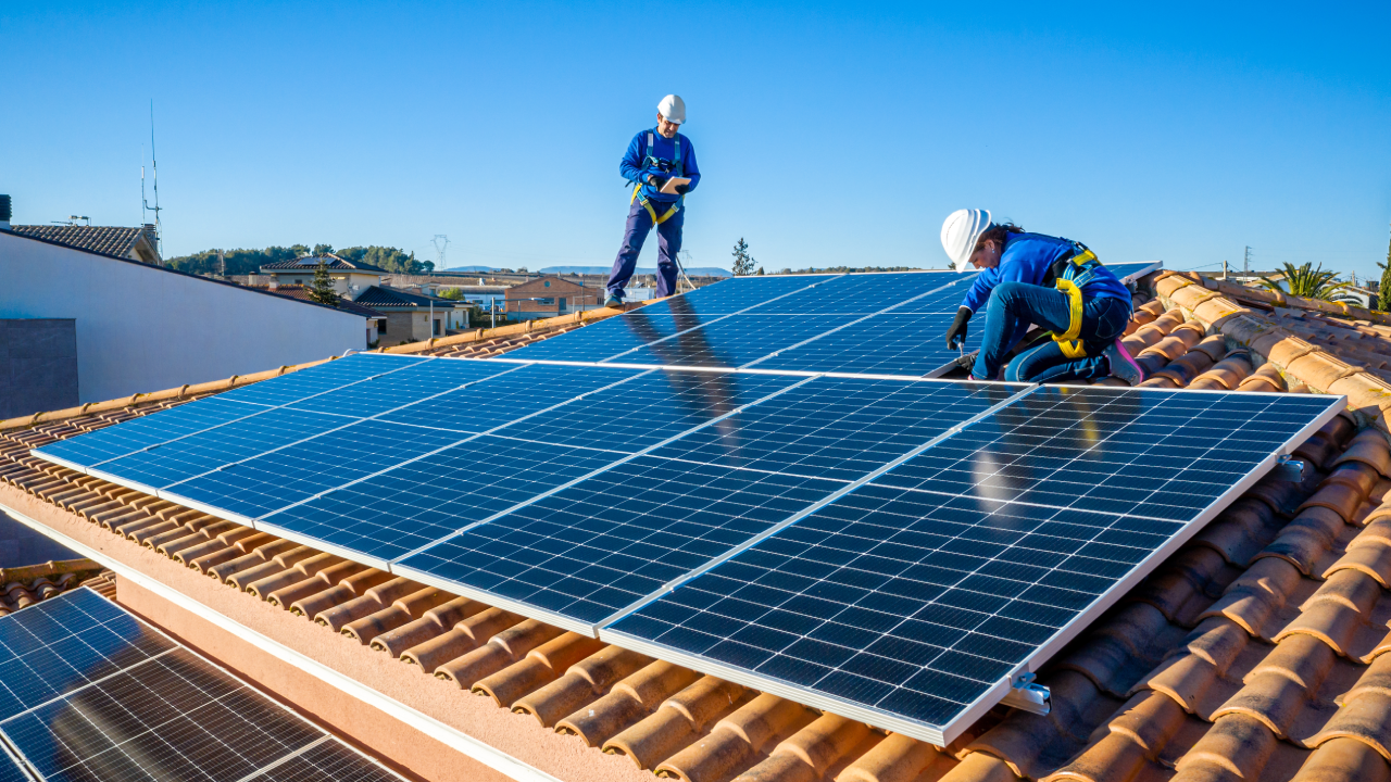 Male and female workers installing solar panels on a roof.