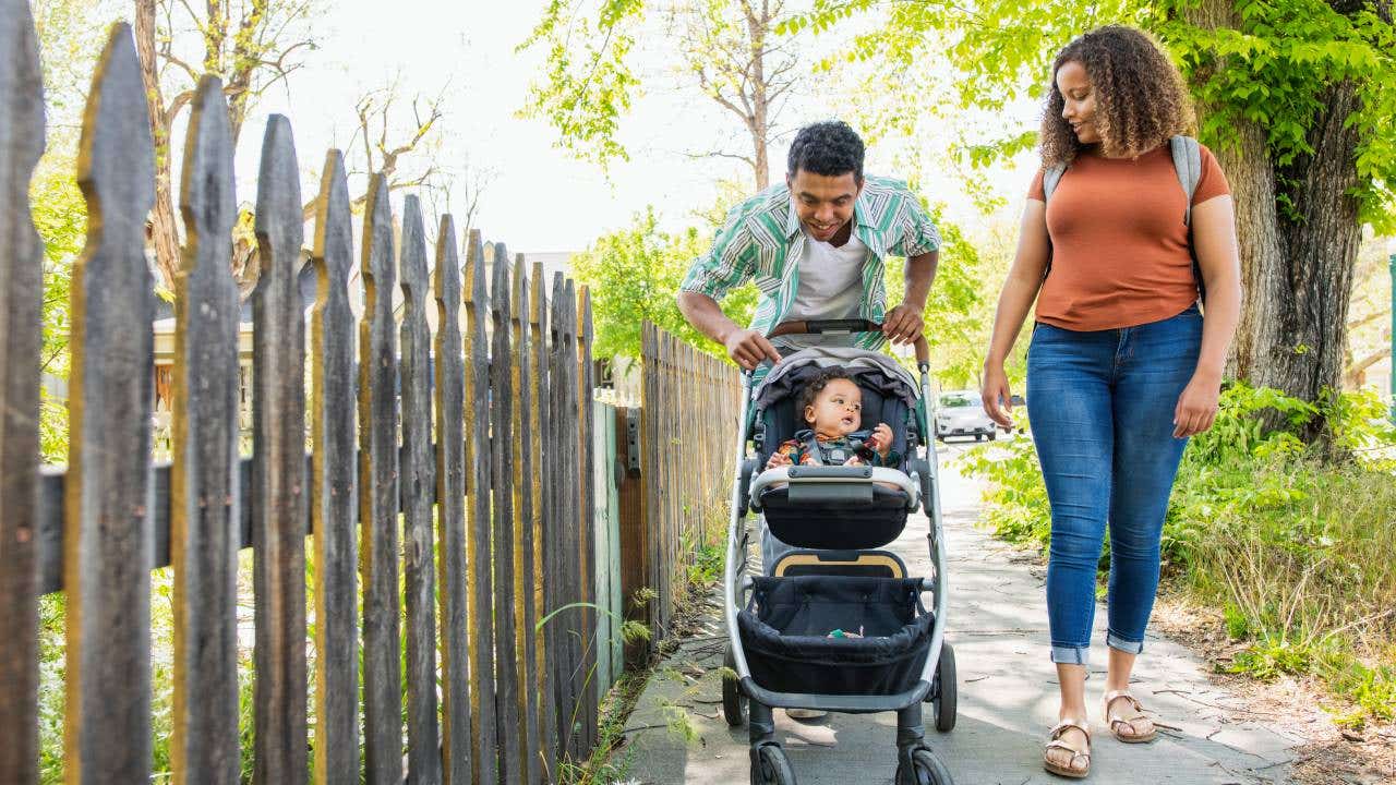 A young couple walks with their child in a stroller.