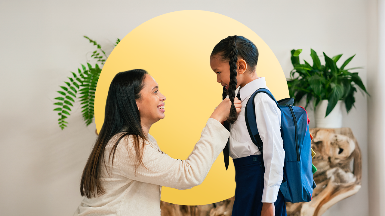 Mom in business clothes kneeling down in front of her daughter, who is wearing a backpack, getting ready to send her off to school