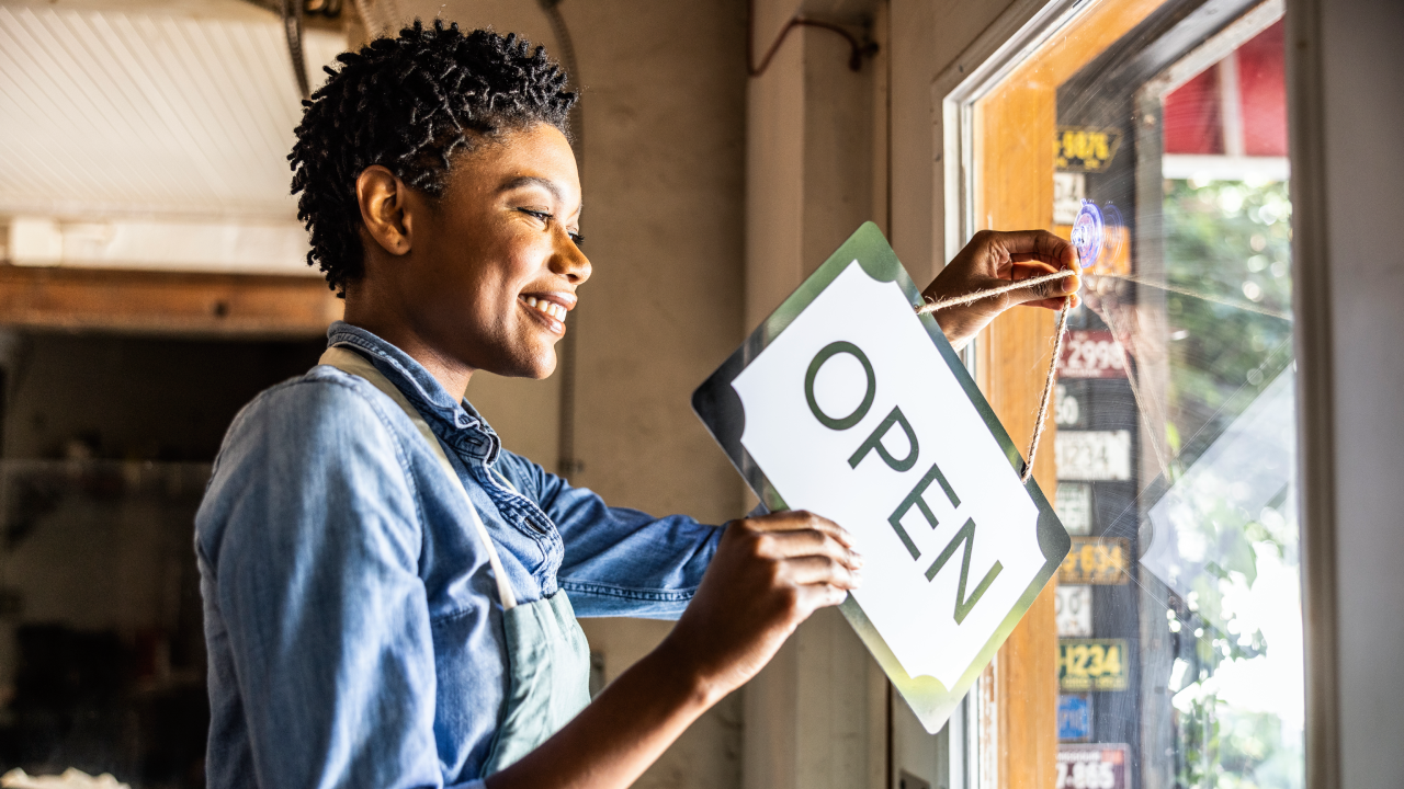 Female small business owner placing open sign in business window
