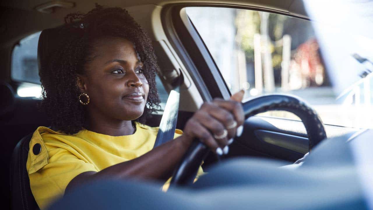 Charming young woman sitting in driver's seat in her car and enjoying a ride